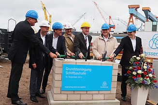 Foto von der Grundsteinlegung. Mehrer Männer stehen um einen Haufen aus Steinen.  