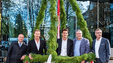 Foto von freundlich schauenden Männern, die unter dem Richtkranzkranz stehen. 