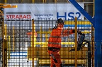 Foto eines Arbeiters hinter einem Bauzaun, der eine Maschine bedient