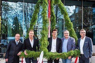 Foto von freundlich schauenden Männern, die unter dem Richtkranzkranz stehen. 