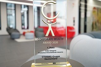 Das Bild zeigt einen Glaspokal auf einem Tisch stehend in einem modernen Büro