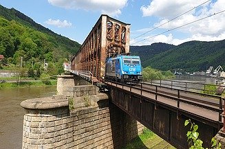 Foto von einer Eisenbahnbrücke aus rostigem Stahl mit einem blauen Zug