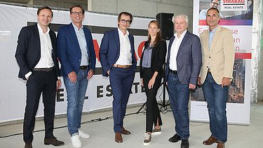 Foto von sechs Personen, die vor einem Transparent der STRABAG Real Estate stehen