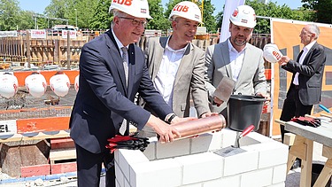 Foto von drei Männern, die eine Röhre halten, die ein gemauert wird.    