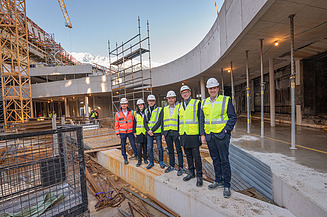 Foto von mehreren Personen mit Bauhelmen und Schutzwesten in einer Baustelle