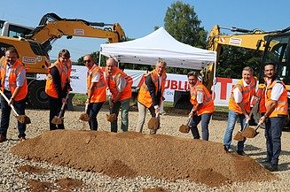 Foto von mehreren Personen bei sonnigem Wetter auf einer Baustelle, die jeweils einen Spaten in den Händen halten und einen symbolischen ‚Spatenstich‘ ausführen