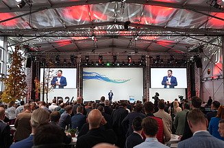 Photo of a ballroom with guests and a stage on which a presentation is running