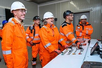 Photo of several people wearing hard hats and orange protective clothing standing at a control panel