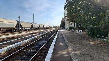 Foto von Bahngleisen bei blauen Himmel, auf einem Gleis steht ein Güterzug mit Waggons
