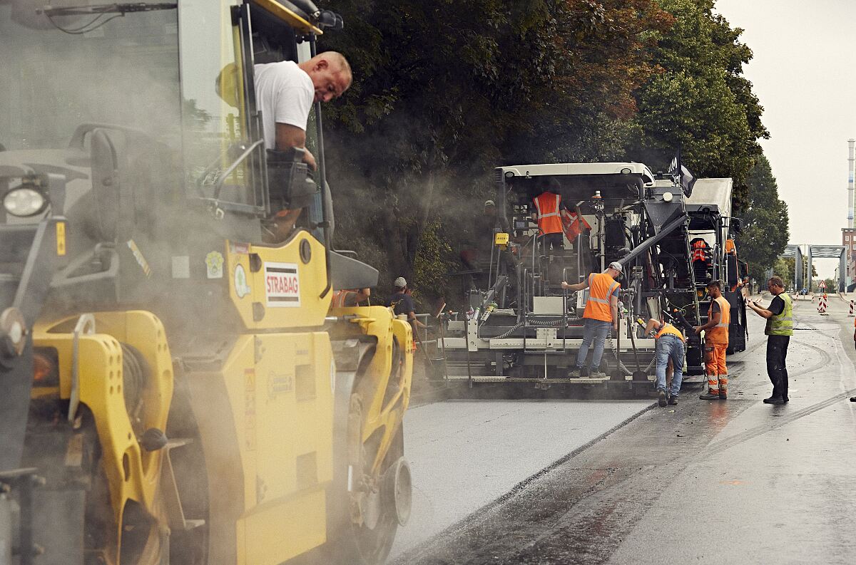 Foto von mehreren Straßenbauarbeitern und zwei Asphaltbaumaschinen bie der Arbeit