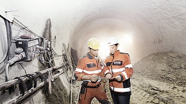 Foto von zwei Tunnelbauarbeitern bei einer Maschine