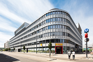 Foto zeigt einen neuen Bürogebäudekomplex, davor eine Straße mit zwei Personen