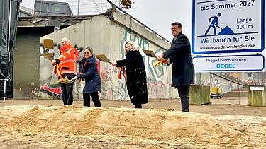 vier Personen schaufeln Sand