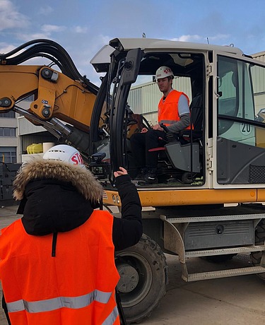 Foto von zwei Personen, die eine sitzt in einem Bagger, die andere steht davor