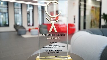 Das Bild zeigt einen Glaspokal auf einem Tisch stehend in einem modernen Büro