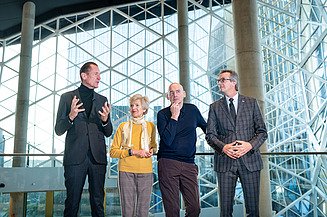 Foto von vier Personen vor einer Glaskuppel, sie schauen nachdenklich.  