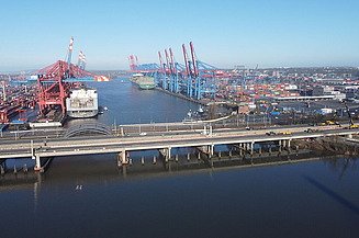 Foto eines Industriehafens davor führt eine Brücke über das Wasser