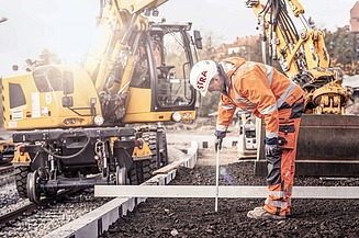 Foto von einem Gleisbauarbeiter in Schutzkleidung, dahinter eine gelbe Gleisbaumaschine