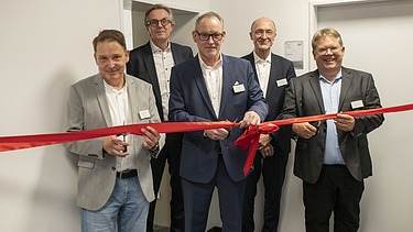 Foto von mehreren Personen die ein Einweihungsband durchschneiden.  