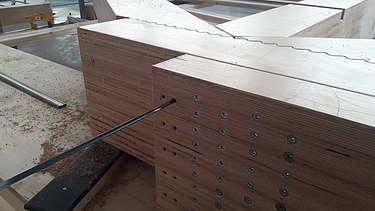 Foto von einer Hartholzplatte, wo mehrere Schrauben gebohrt wurden.   