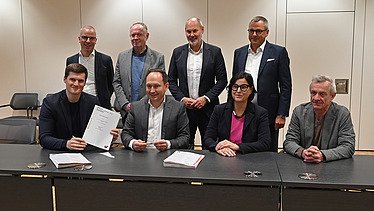 Foto von mehreren freundlich schauenden Personen die an einem Tisch sitzen. 