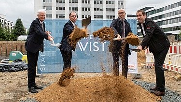 Foto von vier Männern, die mit einem Spatzen, Erde von einem Haufen Erde hochwerfen.  