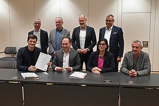 Foto von mehreren freundlich schauenden Personen die an einem Tisch sitzen. 