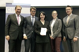 Photo of several people standing, the person in the middle holding a certificate
