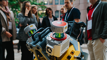 Photo shows an engine in the foreground, behind it some people are looking at it