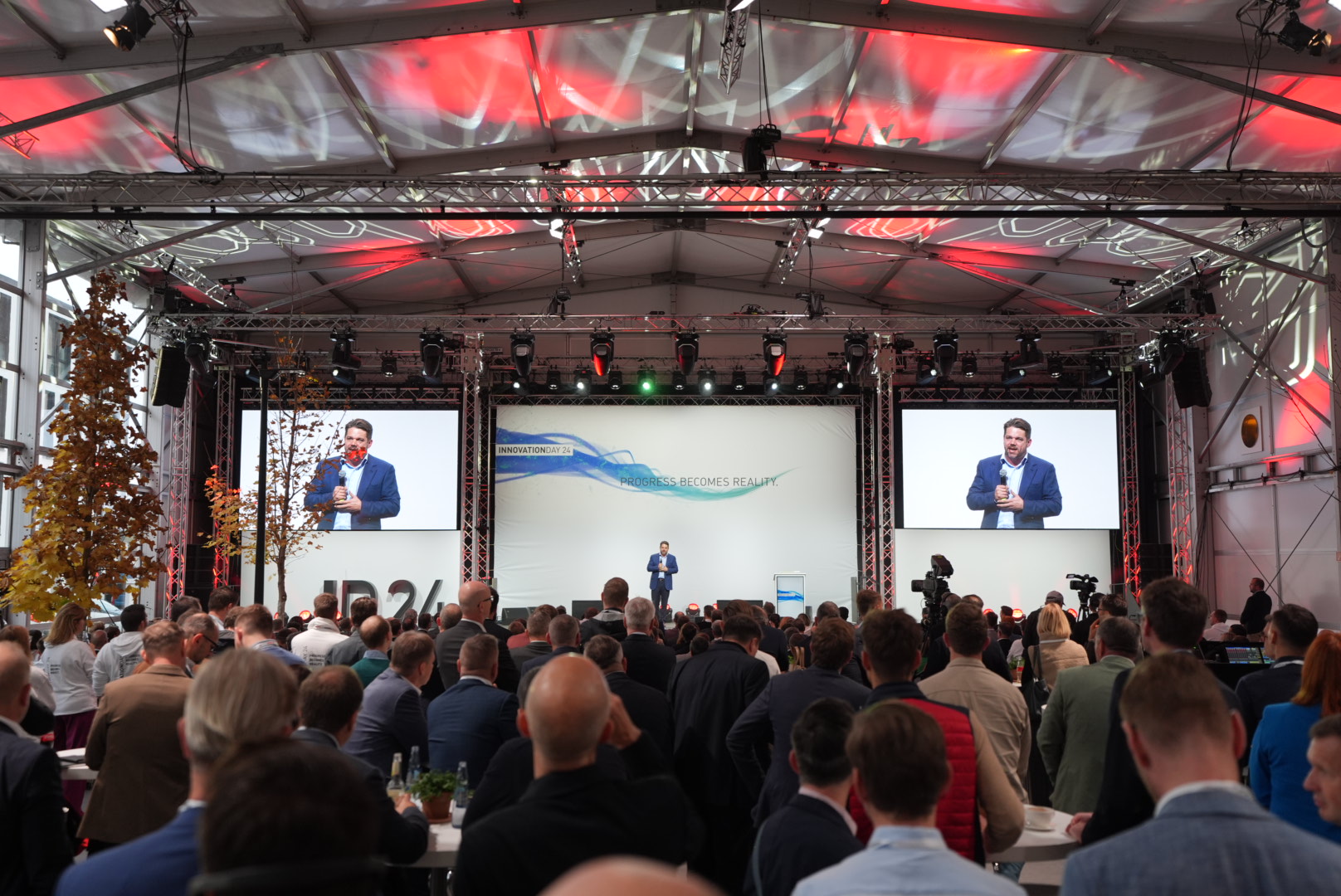 Photo of a ballroom with guests and a stage on which a presentation is running