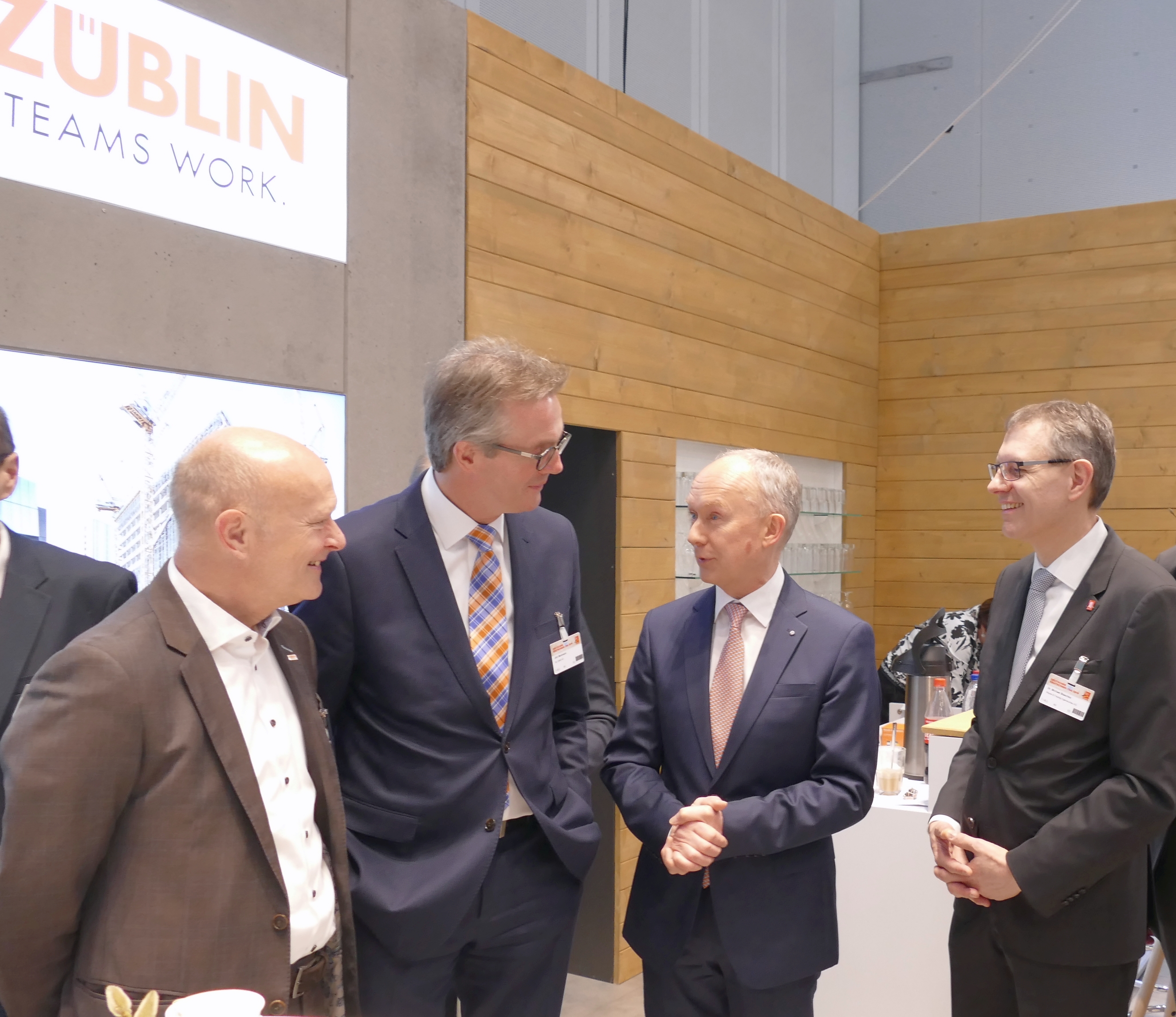 Foto von vier Männern im ZÜBLIN-Stand auf dem Deutschen Bautechniktag 2019 in Stuttgart. Sie lächeln. 