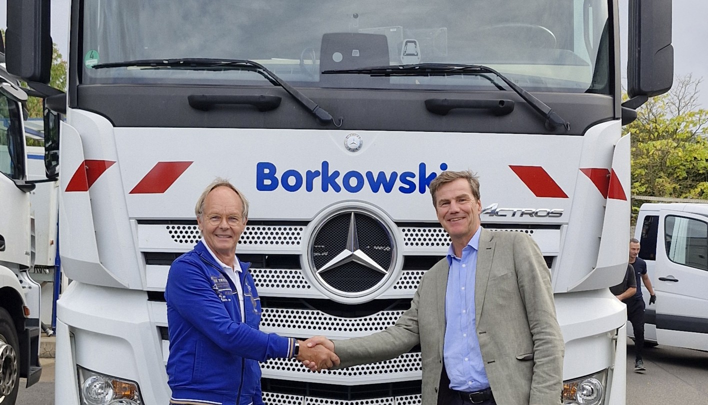 Foto von zwei männlichen Personen, die sich die Hand geben und vor einem LKW stehen mit der Aufschrift Borkowski