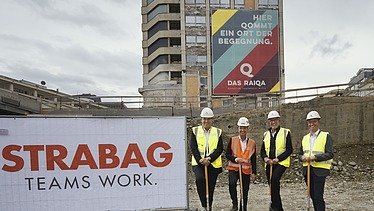 Foto von vier Personen stehen beim Spatenstich vor dem Raiqa Hochhaus, links ist ein STRABAG Transparent