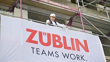 Mann steht auf einem Gerüst einer Baustelle. Vor ihm ist das ZÜBLIN Banner. 