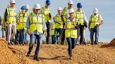 Foto von mehreren Personen in Schutzwesten und Bauhelmen, die auf einem Erdhügel stehen
