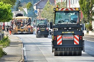 Das Bild zeigt eine gerade Straße auf der mehrere Straßenbaumaschinen hintereinander fahren