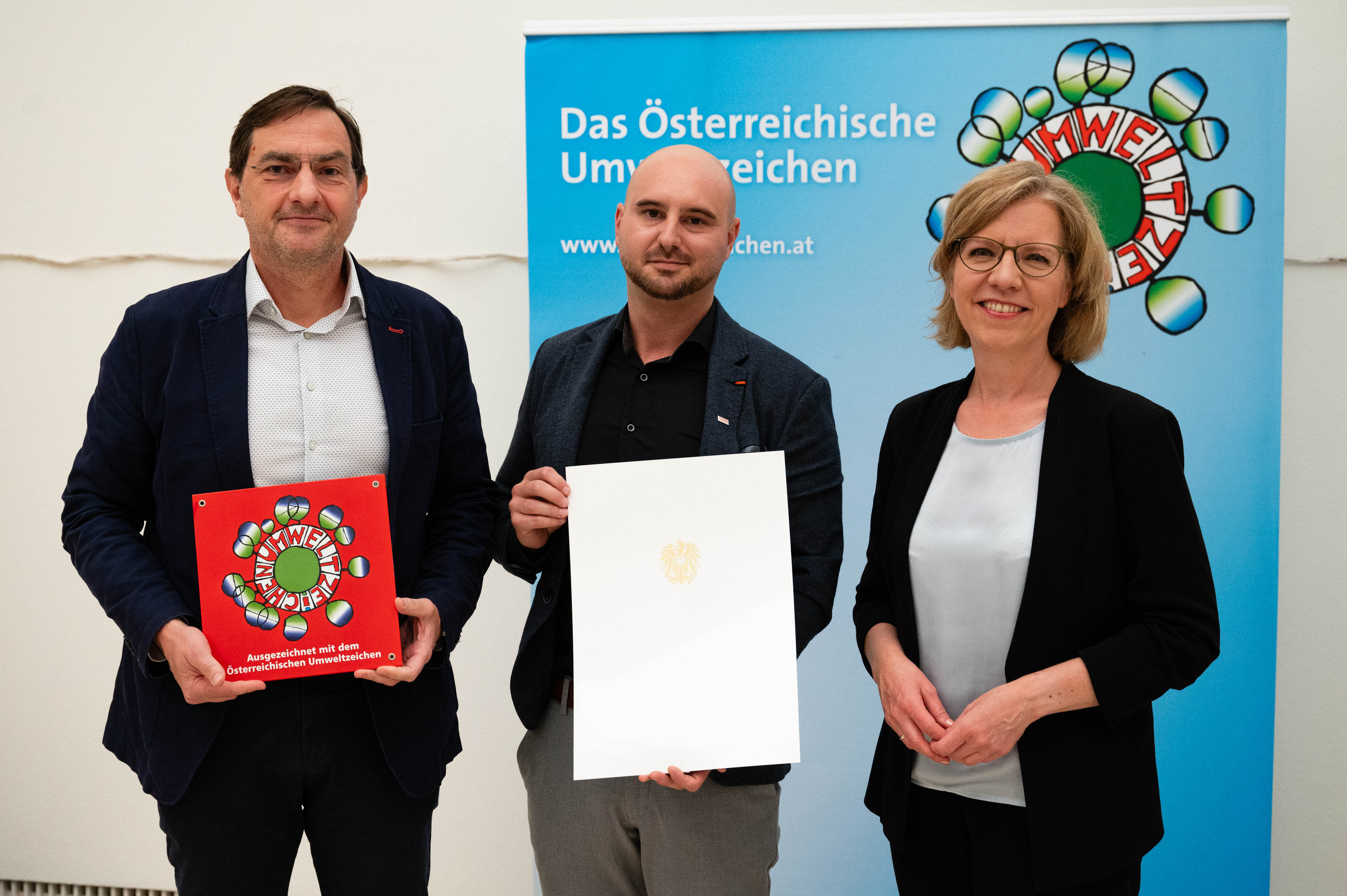 Foto von drei Personen, die beiden links halten jeweils eine Urkunde in den Händen
