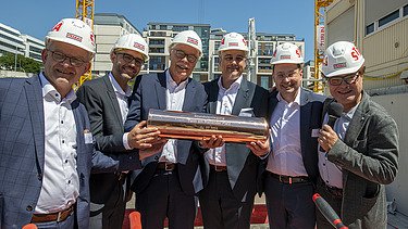 Foto von mehreren Männern auf einer Baustelle, die ein Gefäß in der Hand halten.  