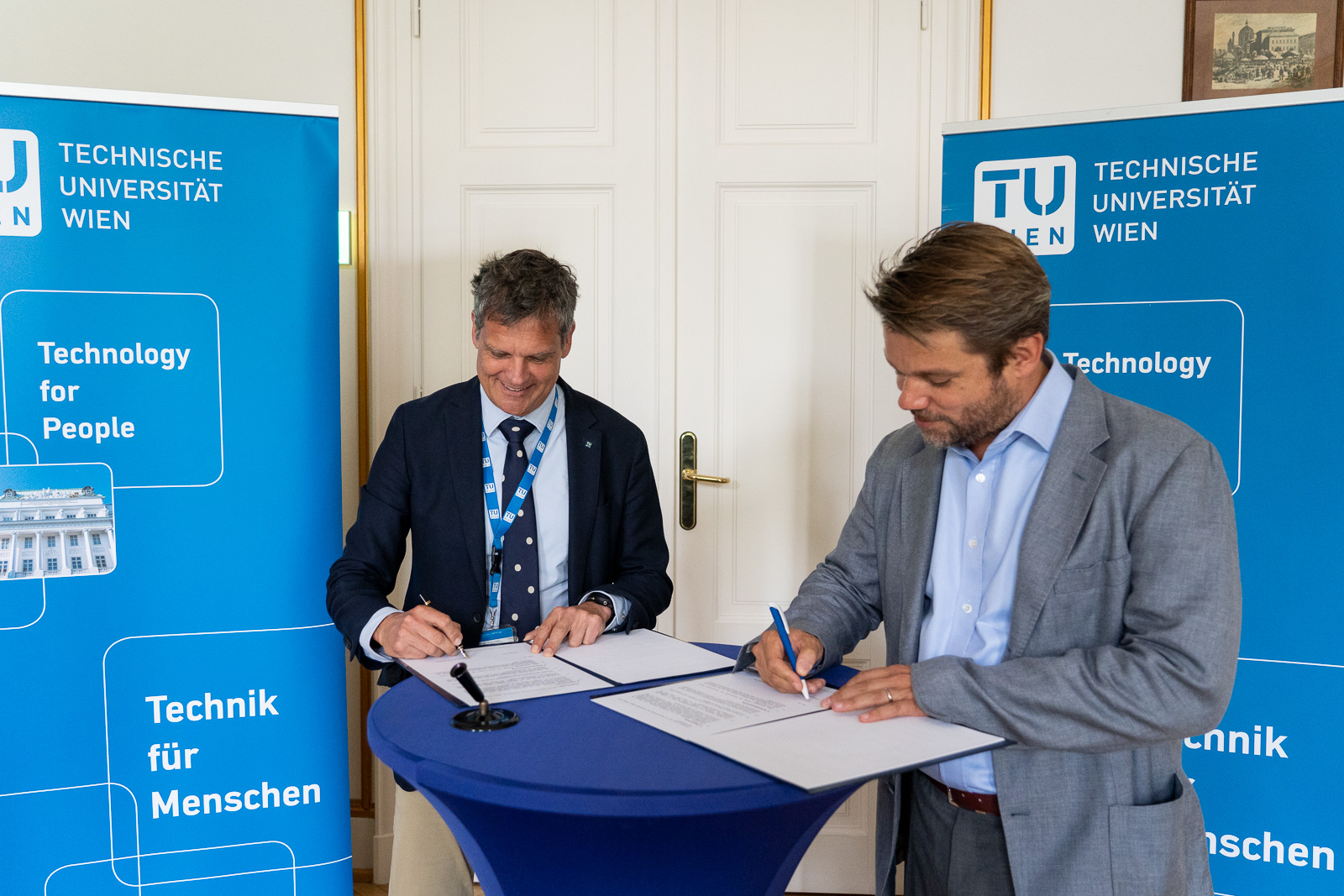 Foto von zwei Personen an einem Stehtisch, die Dokumente unterzeichnen