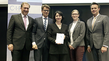 Photo of several people standing, the person in the middle holding a certificate