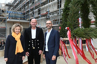 Foto von drei freundlich schauenden Personen auf einer Baustelle. Sie stehen vor dem Richtkranz.  