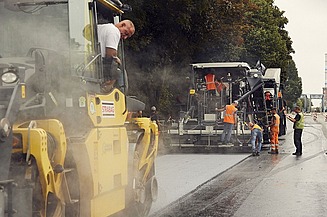 Foto von mehreren Straßenbauarbeitern und zwei Asphaltbaumaschinen bie der Arbeit