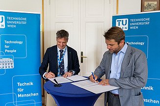 Foto von zwei Personen an einem Stehtisch, die Dokumente unterzeichnen
