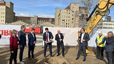 Foto von mehreren Personen im Anzug die eine Röhre vergraben.  