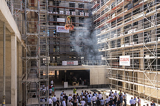 Foto von einer Baustelle, wo der Richtkranz aufgehangen wird. Viele Menschen schauen sich, dies an.      