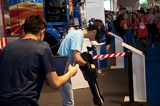 Foto von zwei Personen, die rechte Person hat eine digitale Brille auf und sieht nach unten