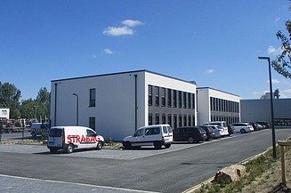 Foto von einem Neubau davor parken einige Firmenfahrzeuge, der Himmel ist blau