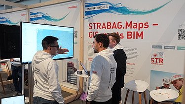 Photo of three people in front of a screen, with a STRABAG banner behind them