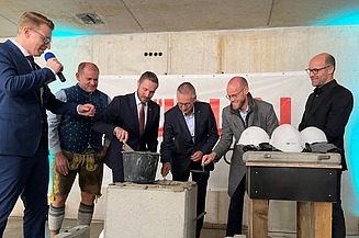 Foto von mehreren Männern im Anzug, die Beton in einen Stein verstreichen. 