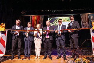 Mehrere Personen schneiden auf einer Bühne ein Band durch